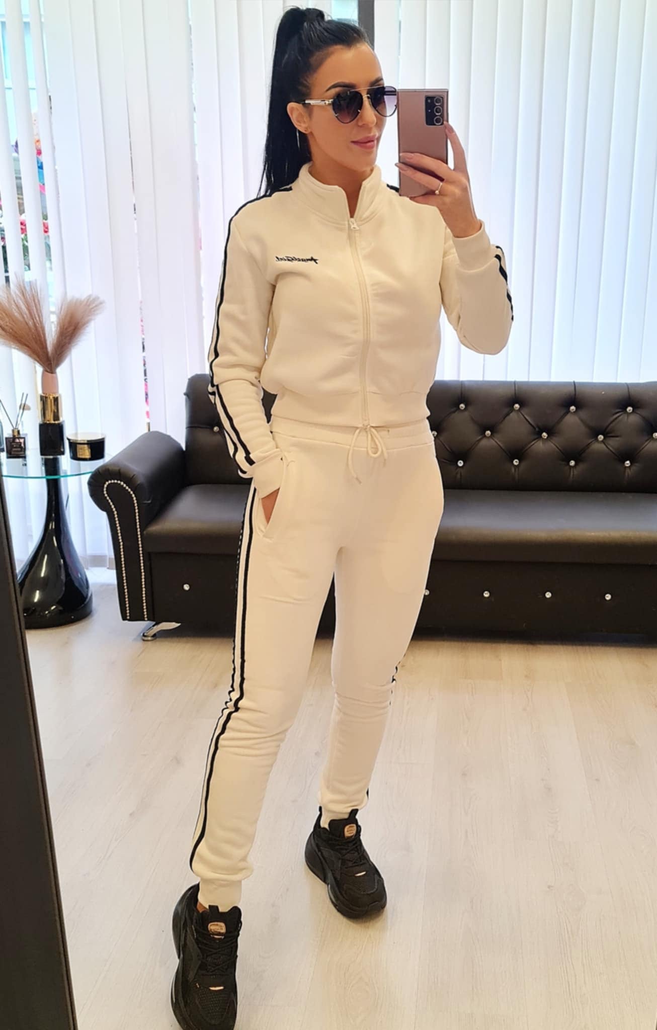 Dame joggedress i fargen hvit, laget av myk bomullsblanding. Sporty design med striper langs ermene og buksene. Tilgjengelig i størrelsene S/M, M/L, L/XL og XL/2XL. Perfekt for fritid, trening og hverdagsbruk.